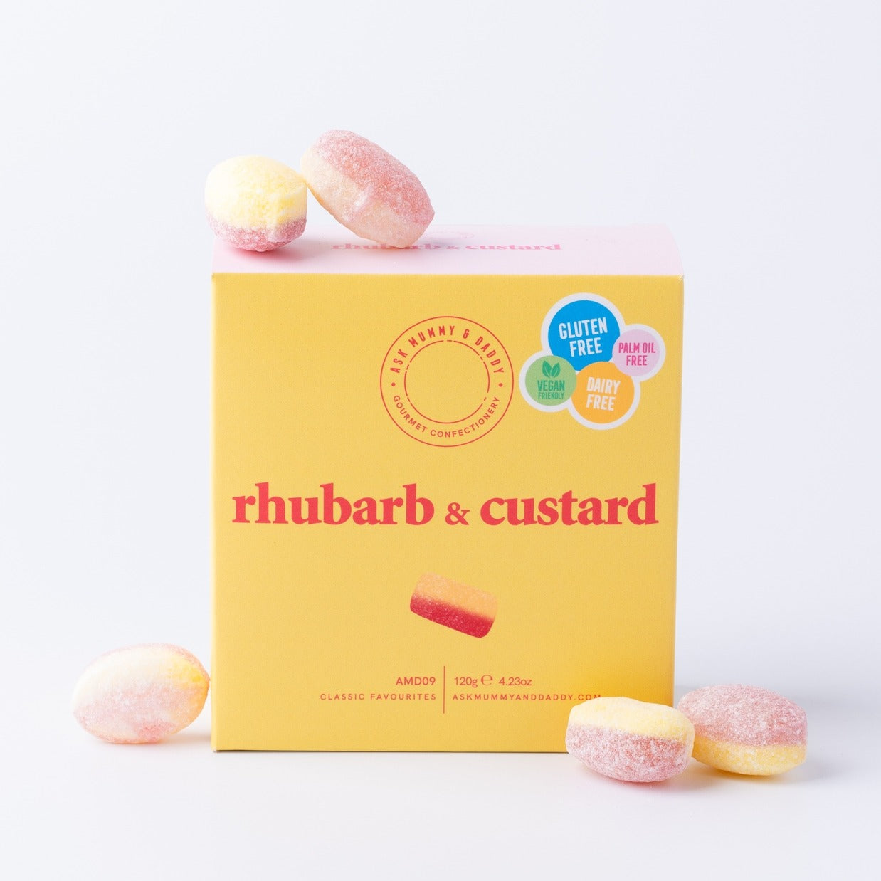 Yellow box of rhubarb and custard sweets with candy pieces around on a white background