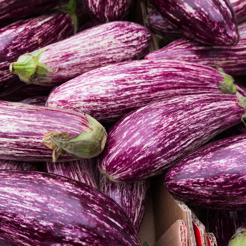 A close-up pile of eggplants with deep purple and white marbled skin, some showing green stems.