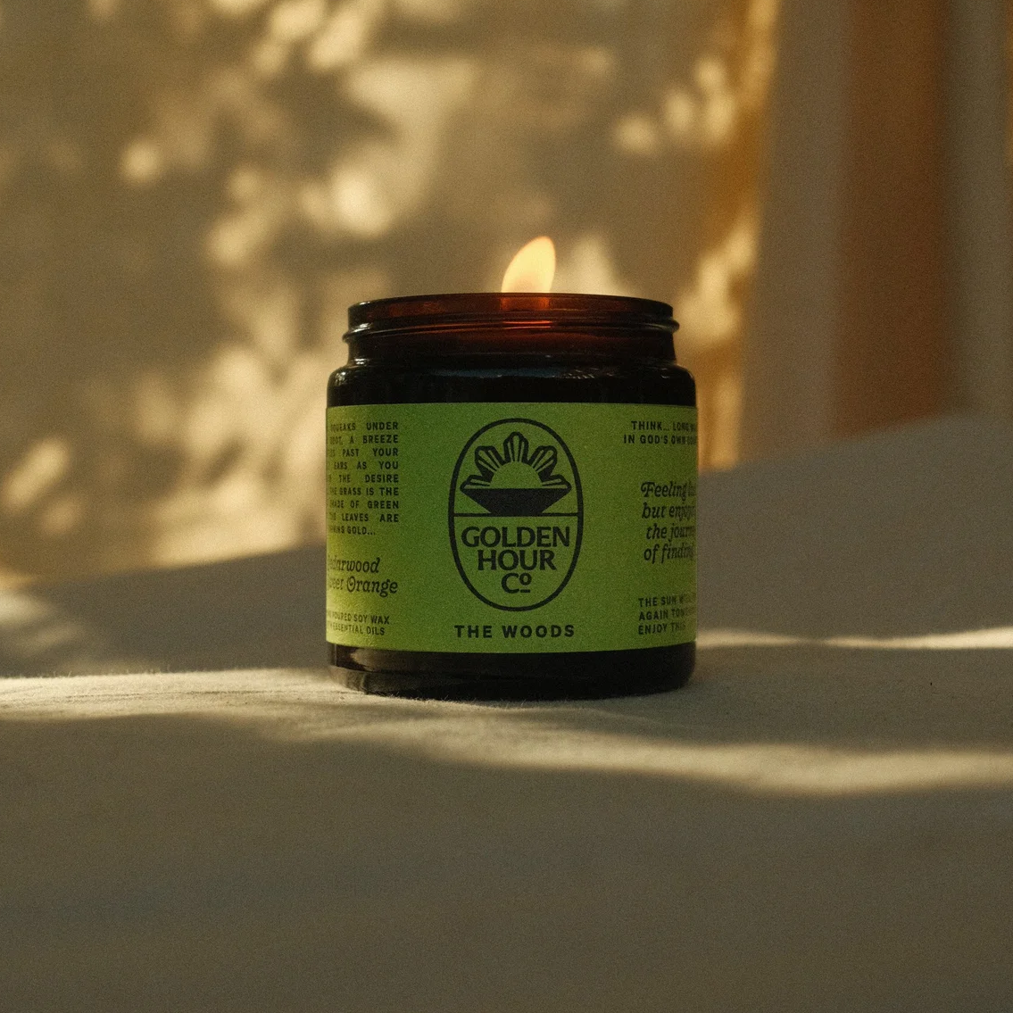 Golden Hour Candle Co. hand poured soy wax candle with cedarwood and orange essential oils with lit with a leafy silhouette in the background