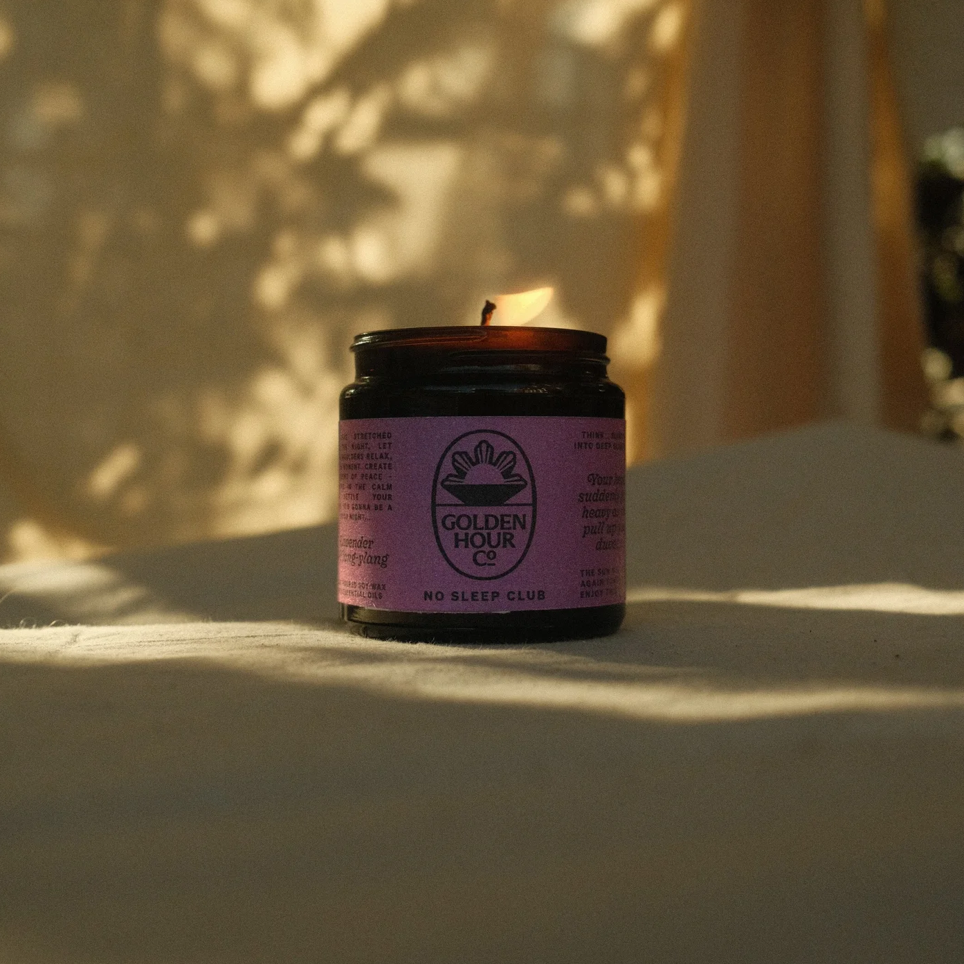Golden Hour Hand Poured Soy Wax Candle in a jar with a pink label on a textured surface with shadows