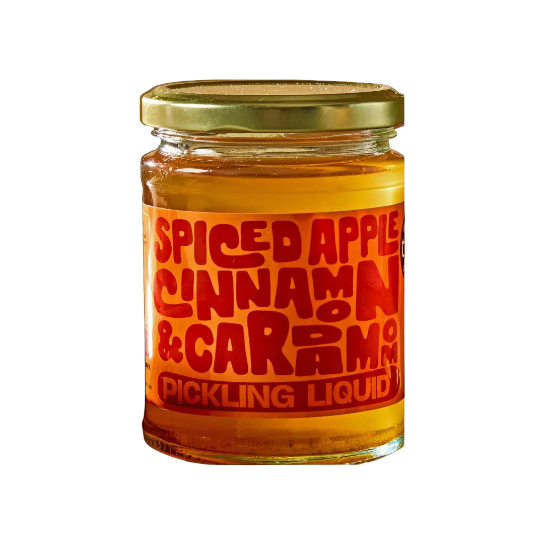 Jar of spiced apple cinnamon & cardamom pickling liquid with a red label on a black background