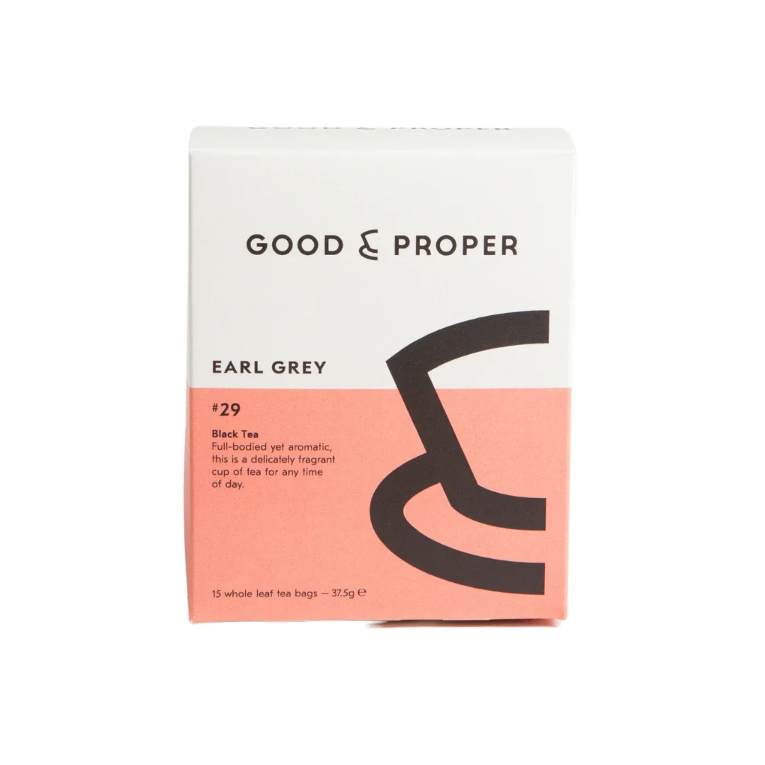 A box of Good & Proper Earl Grey #29 black tea, featuring a white and coral pink color-blocked design with a large black abstract teacup graphic on the front, set against a plain white background.