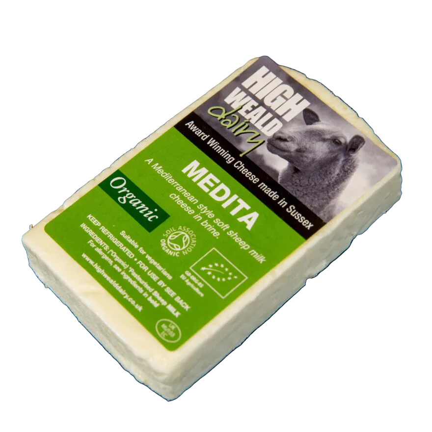 A single wedge of High Wall 2021 Medita organic sheep's milk cheese on a dark textured background, showing the green and black label with a cow graphic.