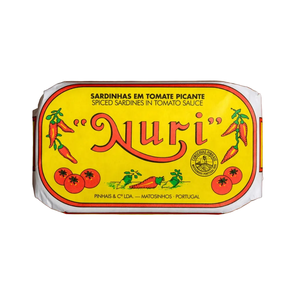 A packaged food product labeled "Nuri" spiced sardines in tomato sauce, shown from above on a wooden surface. The package has a bright yellow label with red lettering and illustrations of tomatoes, carrots, and sardines.