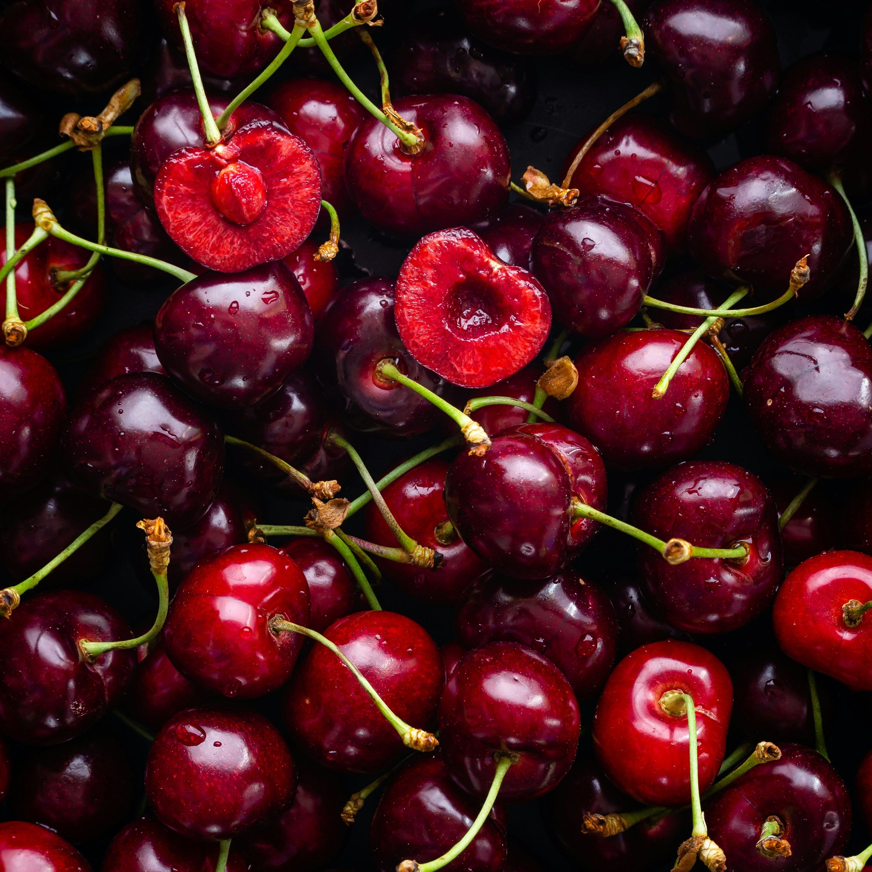 Close-up of a pile of red cherries with green stems.