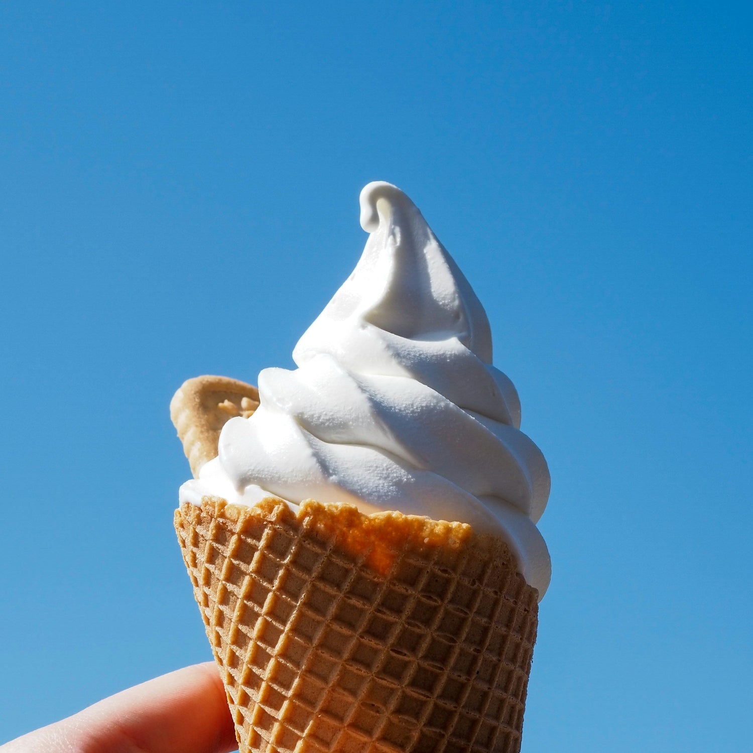 Ice cream cone with white soft serve against a clear blue sky
